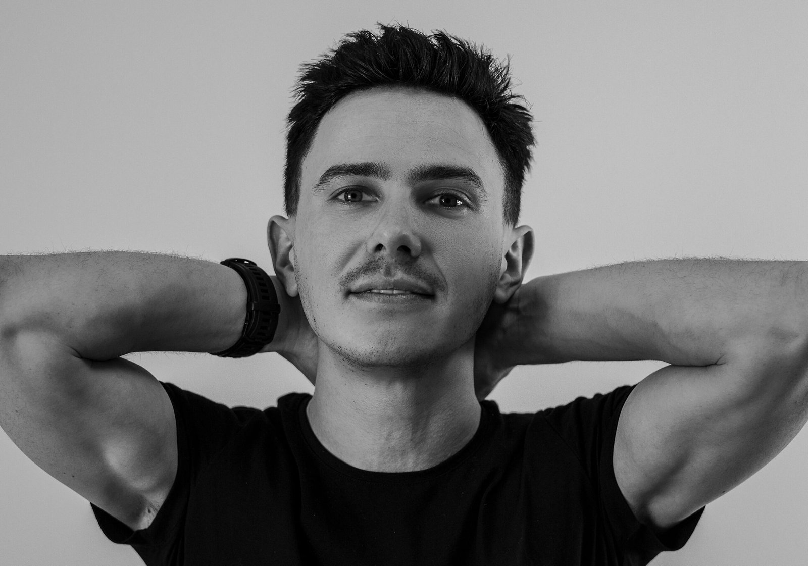 Artistic black and white portrait of a man with short hair posing with arms behind head.